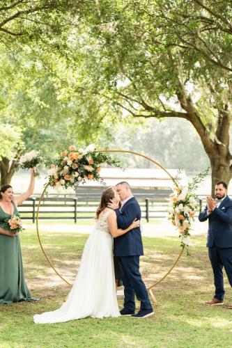 bride and groom first kiss under circle arch during outdoor wedding 